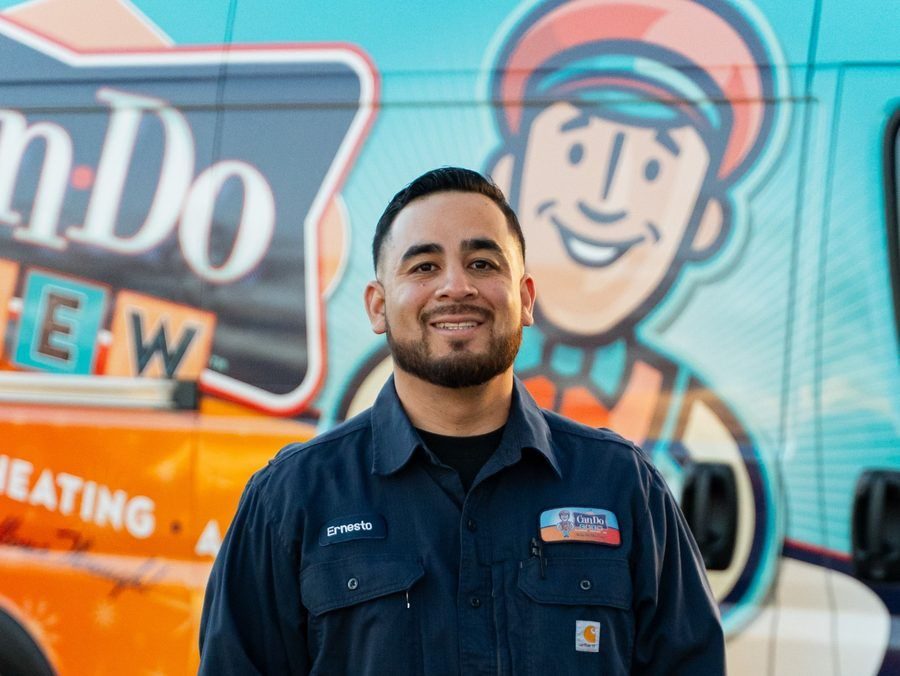 Smiling man in a navy work shirt with the name Ernesto, standing before a colorful mural and orange service vehicle in the background.