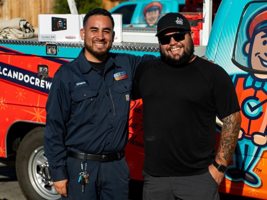 Two men smiling while posing in front of a colorful cartoon-themed rescue vehicle; one in a dark blue uniform with a name tag, the other in a black T-shirt and cap.