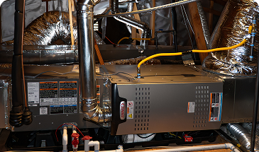 Gas furnace in a utility room with metal ductwork, insulated pipes, and wiring visible overhead.
