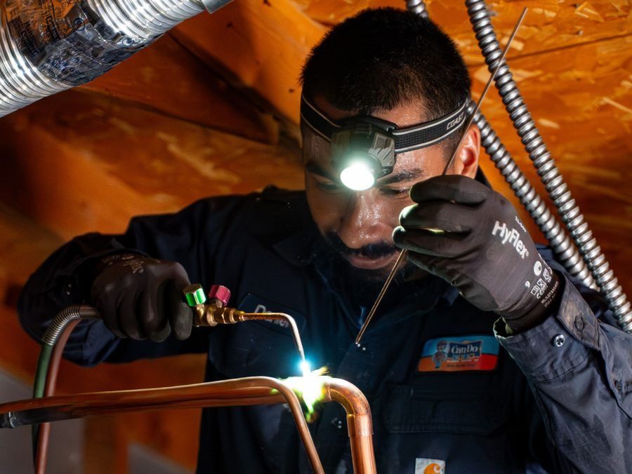 Welder with headlamp fusing copper pipes, sparks flying, wearing gloves and protective gear in a ductwork setting