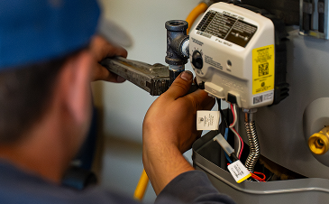 HVAC technician tightening a furnace ignition control module with a wrench, wiring exposed in the foreground