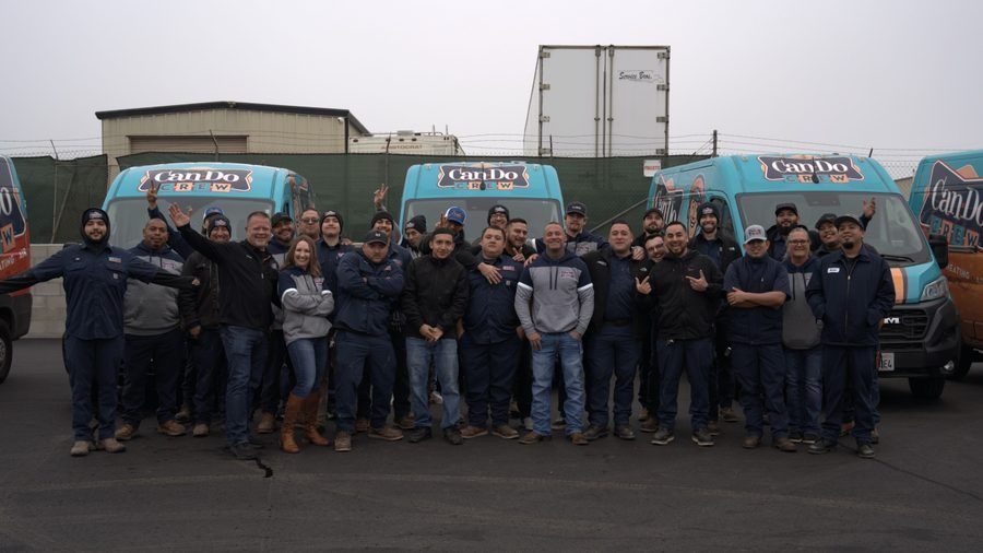 Group of coworkers posing together in front of three turquoise vans with Can Do Crew logos, outdoors on a paved lot.