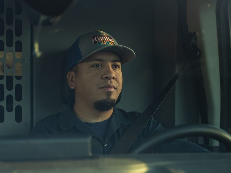 Truck driver wearing a cap and seatbelt, focused while driving in the cab.