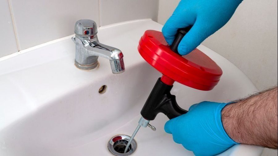 Plumber with a tool aimed down the drain for drain cleaning service.