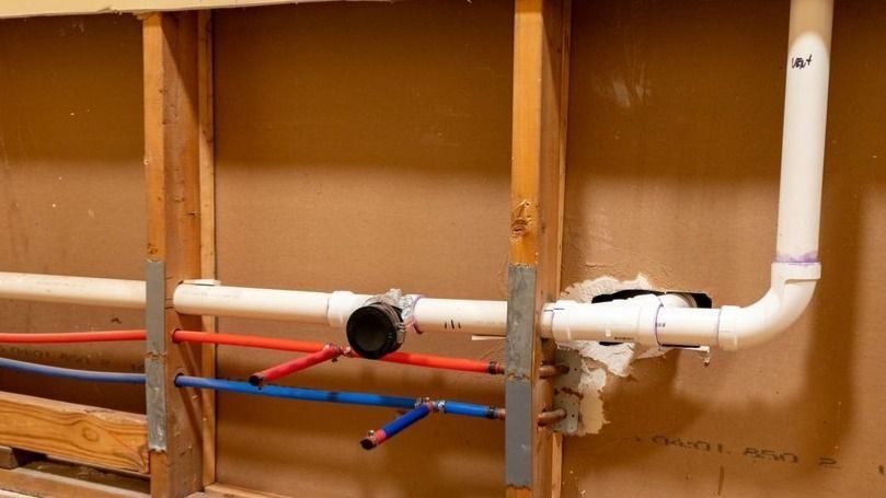 Exposed pipes against a bare wall during leak detection service.