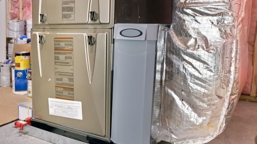 Residential gas furnace installed in a basement, connected to insulated ductwork and air filtration components.