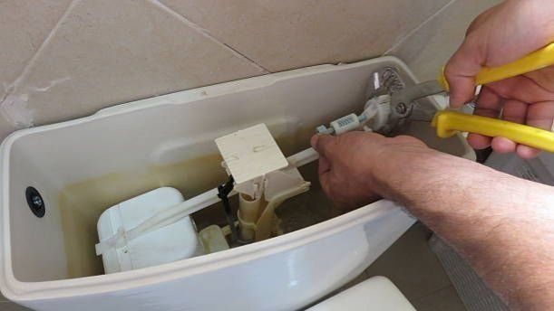 Plumber in open top toilet repairing.